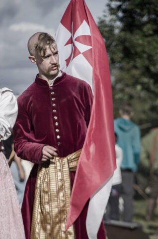 Fundacja Banici Zamojscy Szlachcic na tle husarskiej chorągwi.