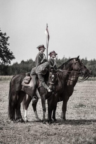 Trzech ułanów na koniach. Jeden z nich karmi konia jabłkiem.